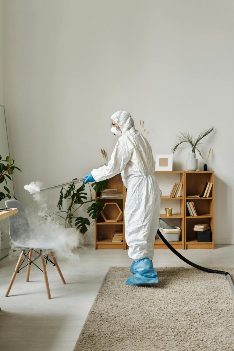 A person in protective suit disinfecting a chair indoors, enhancing hygiene and safety.