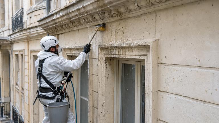 Professionnel nettoyant une façade d’immeuble souillée par des fientes de pigeon avec équipement de protection