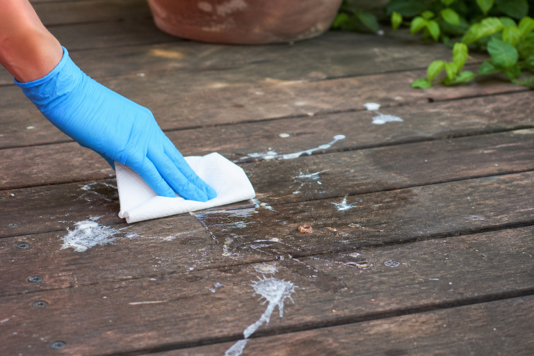 Main gantée nettoyant des fientes de pigeon sur une terrasse en bois avec un chiffon blanc