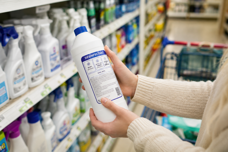 Personne lisant l’étiquette d’un produit désinfectant en rayon pour choisir une solution adaptée à ses besoins d’hygiène.