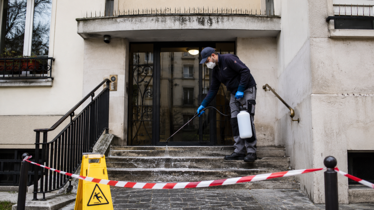 Technicien nettoyant et désinfectant une entrée d’immeuble souillée par les fientes de pigeons avec zone de sécurité balisée