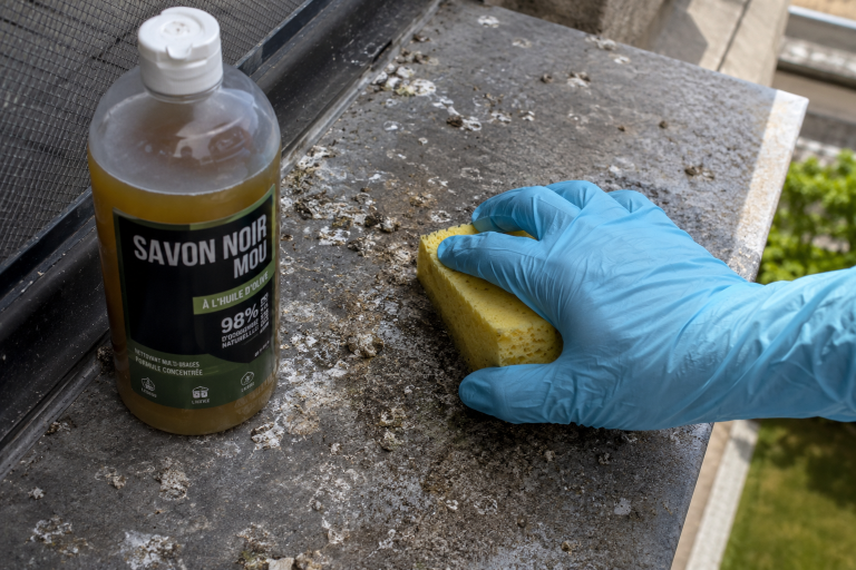 Nettoyage de fientes de pigeon sur un rebord extérieur avec du savon noir et une éponge